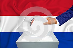 Elections in the country - voting at the ballot box. A man`s hand puts his vote into the ballot box. Flag Paraguai on background