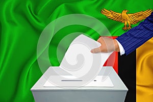 Elections in the country - voting at the ballot box. A man`s hand puts his vote into the ballot box. Flag Zambia on background