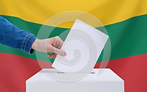 Elections, Lithuania. A hand throws a ballot into the ballot box. The flag of Lithuania on the background. The concept of voting
