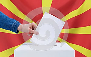 Elections, North Macedonia. Election concept. A hand throws a ballot into the ballot box. Flag of North Macedonia on background