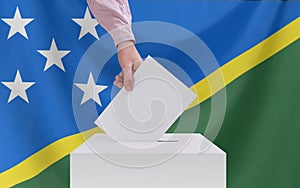 Elections, Solomon Islands. Election concept. A hand throws a ballot into the ballot box. Flag of Solomon Islands on background