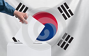 Elections, South Korea. The concept of elections. A hand throws a ballot into the ballot box. The flag of South Korea on the