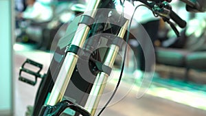 Electric bicycle details closeup, front wheel, shock absorbers on steering tube. With unfocused people behind
