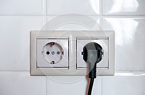 Electric black plug. Two sockets on a background of white tiles.