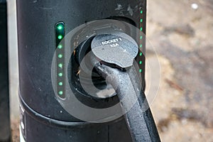 Electric car cable plugged into street charging station connector, green lights on, closeup detail