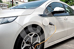 The electric car is charged from the mains, the cable from the charging station photo