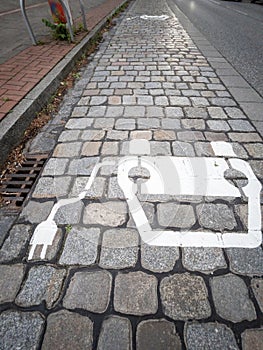 Electric car charging sign painted on paving stones on a city street.