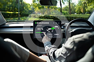 Electric car driver checks battery charging status app screen in car innards