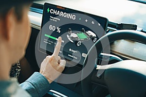 Electric car driver checks battery charging status app screen in car innards