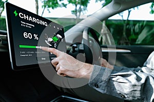 Electric car driver checks battery charging status app screen in car innards