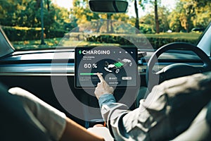 Electric car driver checks battery charging status app screen in car innards