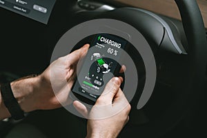 Electric car driver checks battery charging status app screen in car innards