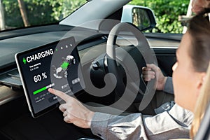 Electric car driver checks battery charging status app screen in car innards