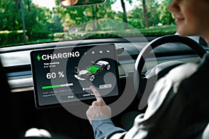 Electric car driver checks battery charging status app screen in car innards