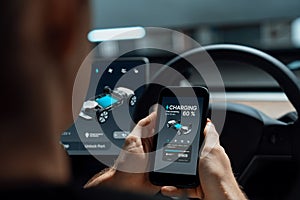 Electric car driver checks battery charging status app screen in car innards