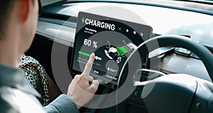 Electric car driver checks battery charging status app screen in car innards