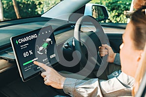 Electric car driver checks battery charging status app screen in car innards