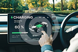 Electric car driver checks battery charging status app screen in car innards