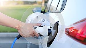 Electric car or ev is charging at station . man use the white power cable and plug on nature background. eco and clean energy