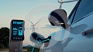 Electric car recharging energy from charging station in wind turbine farm.Peruse