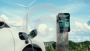 Electric car recharging energy from charging station in wind turbine farm.Peruse