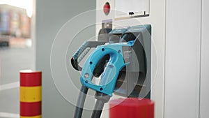 Electric charging station with blue and black power cords. Blurred background of urban area. Eco friendly transport and