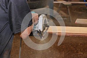 Electric circular saw is being sawed a piece of wood by senior worker in carpentry workshop.