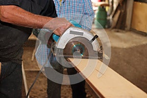 Electric circular saw is being sawed a piece of wood by senior worker in carpentry workshop.