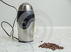 An electric coffee-mill on a white table, next to a handful of roasted coffee beans