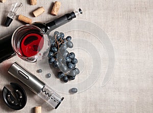 Electric corkscrew in steel gray. On a gray linen background. Near a glass, several corks, a bunch of grapes and a bottle of wine
