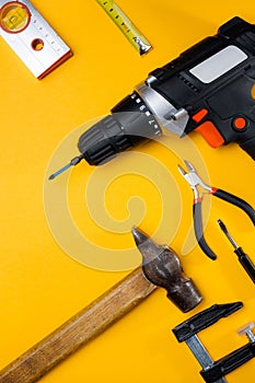 Electric drill and drill bits on a yellow background. Hammer drill or screwdriver flat lay. Top view of professional instrument.