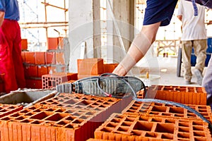 Electric drill tool on pile of red blocks, worker builds wall with bricks and mortar, building site