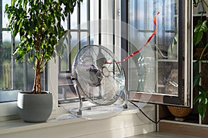 Electric fan with red wriggle ribbon designed to cool air and supply wind is located on windowsill photo