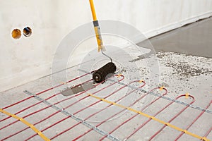 Electric floor heating system installation in new house. Closeup of concrete, roller and red electrical wires.