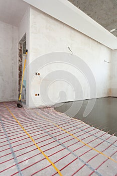 Electric floor heating system installation in new house. Room with white walls, cement and electrical wires