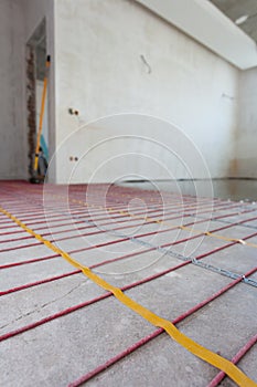 Electric floor heating system installation in new house. Room with white walls, cement and electrical wires