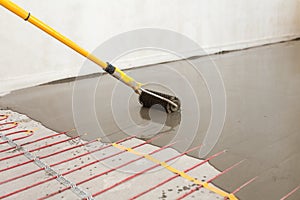 Electric floor heating system installation in new house. Worker align cement with roller.