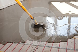 Electric floor heating system installation in new house. Worker align cement with roller.