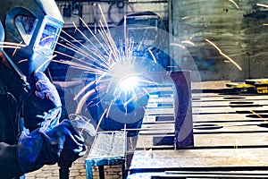 An electric and gas welder in an electromechanical workshop welds a metal structure at a mechanical assembly site
