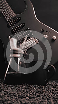A electric guitar on a black, silver background, with a coffee brewing jug in front of it and a black coffee mug on coffee beans