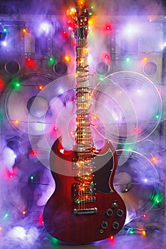 Electric guitar with festive Christmas lights and music speakers in smoke