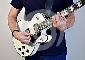 Man playing a white electric guitar with humbucker pickups.