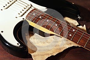 Electric guitar and old music notes on wooden background closeup