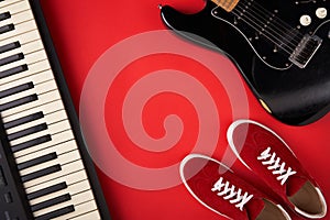 Electric guitar, synthesiser and red stylish sneakers, on red background