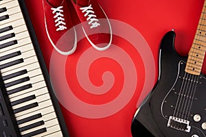 Electric guitar, synthesiser and red stylish sneakers, on red background