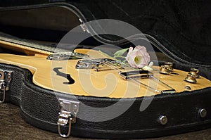 Electric guitar with volume and tone control knobs in black guitar case and flower