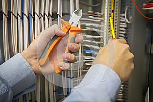 Electric installation work. Screwdriver and pliers in hands of an electrician on background of electric cabinet.