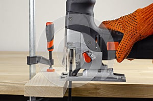 Electric jigsaw. Clamp. Woodworking power tools. Jigsaw in hand. Wooden planks. To the Workshop. On a wooden table. Desktop. Workp