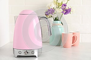 Electric kettle, bouquet and cups on counter in kitchen