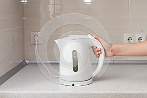 Electric Kettle in hand on the background of the kitchen